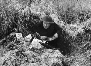 eat British soldier eating Christmas meal in his slit trench w. holiday cards from home propped up outside